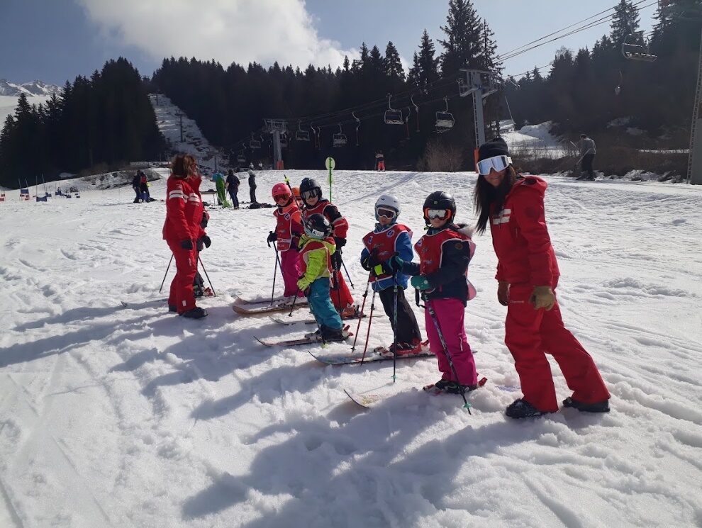Enfants en combinaisons rouges alignés sur la neige, monoskis aux pieds