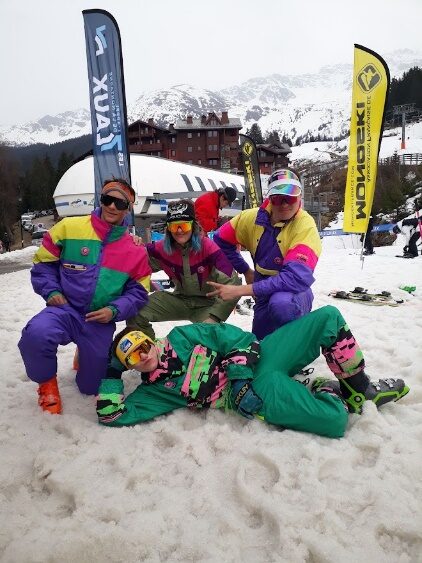 Groupe de riders en combinaisons fluo assis dans la neige devant les oriflammes des 7 Laux